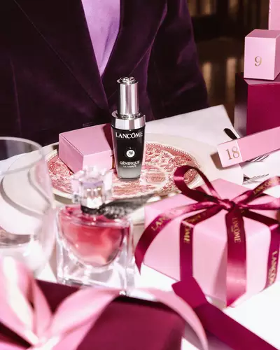 Bir kutlama sofrasında duzenlenmiş Lancome guzellik urunleri ve pembe hediye kutuları.