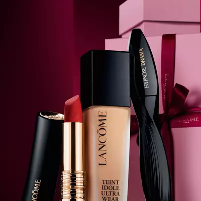 Lancome'un L'Absolu Rouge mat ruju, Teint Idole Ultra Wear fondoteni ve Hypnose Drama maskarasının, luks, koyu kırmızı bir yılbaşı fonunda sunulan zarif naturmort kompozisyonu.