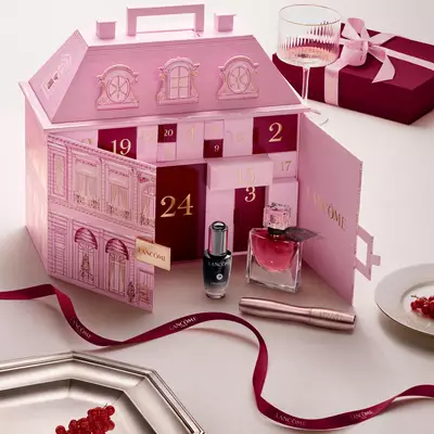 Guzellik urunleri ve kırmızı bir kurdele ile sergilenen, şehir evi şeklinde tasarlanmış acık pembe Lancome Advent Calendar.