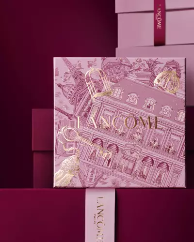Koyu kırmızı bir arka plana karşı, pembe ve koyu kırmızı hediye kutularından oluşan bir yığının onunde duran pembe Lancome yılbaşı hediye kutusu gorseli.