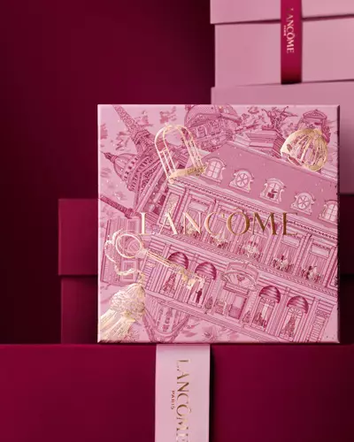 Koyu kırmızı bir arka plana karşı, pembe ve koyu kırmızı hediye kutularından oluşan bir yığının onunde duran pembe Lancome yılbaşı hediye kutusu gorseli.