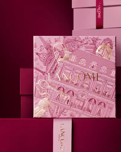 Koyu kırmızı bir arka plana karşı, pembe ve koyu kırmızı hediye kutularından oluşan bir yığının onunde duran pembe Lancome yılbaşı hediye kutusu gorseli.