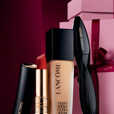Lancome'un L'Absolu Rouge mat ruju, Teint Idole Ultra Wear fondoteni ve Hypnose Drama maskarasının, luks koyu kırmızı bir yılbaşı arka planına karşı zarif bir urun cekimi.